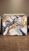 Front view of large abstract painting on stretched canvas with wood frame in black, gray, white, and gold tones.