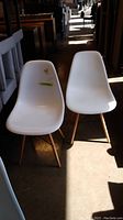 Photo showing two white plastic molded chairs with wooden legs positioned side by side in a well-lit hallway.