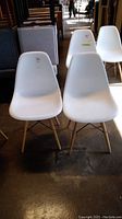 Pair of white molded plastic chairs with wooden legs and black metal braces, showing front view and shadow on floor.