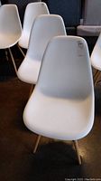 Two white molded plastic chairs with wooden legs shown from front and side angles