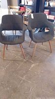 Two mid-century modern style chairs with charcoal linen upholstery and wooden legs seen from the front and side.