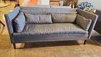 Front view of the grey upholstered sofa showing cushions and wooden legs.
