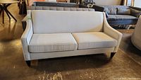 Full front view of cream fabric sofa with two seat cushions and dark wooden legs