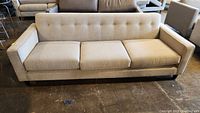 Front view of beige three-seat sofa with loose cushions and button-tufted back