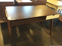 Front angled view of wood desk showing top, front drawer, open storage, and legs.