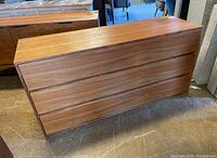 Perspective front view of walnut veneer three drawer dresser on showroom floor