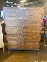 Front view of dresser showing five drawers with horizontal metal handles and walnut veneer finish