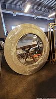Full view of the large round mirror with textured and ridged frame with visible wear and scratches.