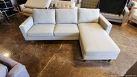 Front-angle view of light gray upholstered sofa with ottoman on wooden legs.