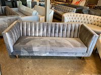Front view of grey velvet three seater couch showing vertical tufted backrest and wood legs.