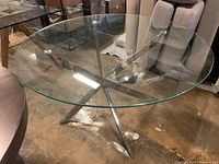 Top view of the round clear glass table top with reflective metal base visible underneath, showing the intersection of metal supports.