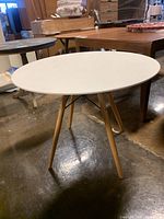 Side angle view of round white wood table showing wooden legs and black metal wire supports.