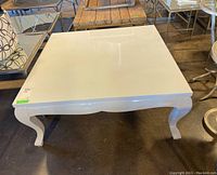 Square white gloss coffee table with curved legs, visible scuffs on top surface.
