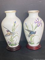 Pair of white porcelain vases decorated with bird and floral motifs, each on a wooden base with gold rim accents.