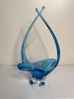 Front view showing the full blue glass dish with upward curved arms crossed at the top and clear footed base.