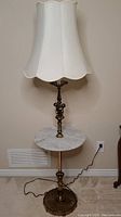 Full view of the brass floor lamp with white scalloped fabric lampshade and round marble tabletop with brass base and stand.