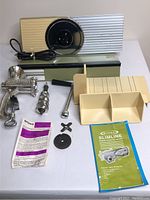 Electric meat slicer with blade cover, sliding platform, food pusher and instruction manual, alongside vintage hand mincer parts spread on table