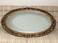 Full view of large oval decorative mirror showing ornate gold frame and clear mirror surface.