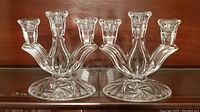 Pair of clear glass candelabras with a pinwheel pattern on bases and three arms to hold candles, shown side by side.
