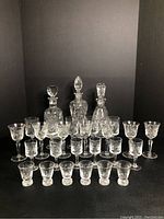 Full view of all Pinwheel patterned etched glassware including 3 decanters with stoppers, various wine, sherry/port, and liqueur glasses arranged by size and type.