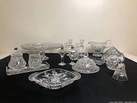 Photo showing entire Pinwheel pattern glassware lot arranged on black fabric background, including cake plate, candle holders, cream and sugar set, gravy boat, pickle tray, bell, salt and pepper shakers, and napkin holder.