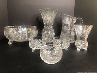 Full group of seven clear pinwheel crystal pieces on black background showing bowl, pitcher, vases, rose bowl, and footed bowls.