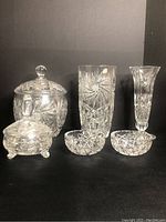 Photo showing entire lot of clear pinwheel cut crystal decorative glassware including vase, cookie jar, candy dishes on black background