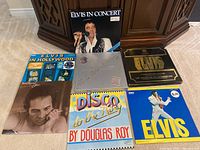 Photo showing 7 vinyl records and box sets arranged side by side with a mix of colorful and monochrome covers, featuring Elvis Presley, Douglas Roy, and Merle Haggard.
