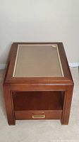 Top view of one wooden end table showing cane panel under glass top and wooden drawer below.