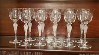 Full view of 11 crystal wine glasses with ballerina stems lined up on a shelf.