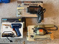 Lot showing three electric tools: Black & Decker Heat'n Strip Electric Paint Remover and Heat Gun in box, Mastercraft Dual Heat Soldering Tool, and Black & Decker Finishing Sander, all with cords visible.