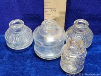 Four vintage clear glass ink well bottles with varied shapes and sizes shown against a ruler for sizing.