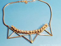 Full view of gold tone geometric necklace with triangular shapes and rhinestone chain detail