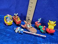 All vintage Looney Tunes diecast and vinyl figures including Pikachu in various vehicles and poses arranged next to a ruler for size reference.