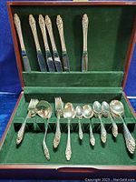 Complete view of the flatware pieces organized inside a green felt-lined wood canteen. The flatware includes knives, forks, soup spoons, and teaspoons featuring floral designs on the handles.
