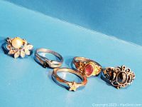 Five vintage Avon rings displayed on blue background, showing various styles and details.