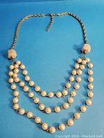 Full view of the triple strand faux pearl necklace with gold-tone chain and white cube beads near the clasp.
