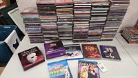 Over 100 compact discs stacked in rows on a table with jewel cases upright, showing the spines in the back with a few albums displayed face up in front.