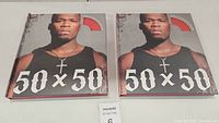 Two closed, identical hard cover books showing front cover with image of 50 Cent and title '50 x 50'.