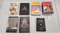 Seven books including Alice editions, Harry Potter, and Tolkien titles arranged in two rows.