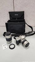 Photo showing Pentax camera with lens, extra lens, camera bag, and lens ring adapter laid out on a surface.