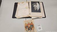 Photo showing the open scrapbook with visible pages including documents and a vintage programme beside it.