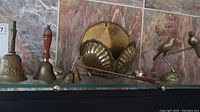 Glass shelf showing brass handbells, snuffers, birds on a branch, shell decorations, round brass plate, and wall rack.