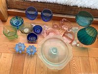 Overview of the full collection showing various colored glass items including bowls, candle holders, and goblets.