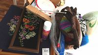 Photo showing knitting needles, yarn, needlepoint hoop, fabric pouch, craft adhesive spray, and framed floral needlepoint images.
