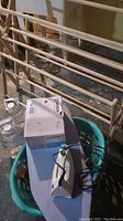 Photo shows green laundry basket holding damaged iron and a small ironing board, with wooden drying rack in background.