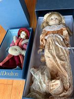 Photo showing two Royal Doulton dolls in original blue boxes with detailed clothing and delicate facial features.