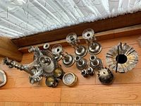 Top-down angled view showing multiple silver-plated candle holders, including candelabra, salt and pepper shakers, and smaller candle holders arranged on a wooden floor.
