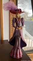Front side view of the Thomas Kinkaid figurine showing detailed purple Victorian-style dress, large feathered hat, and umbrella.