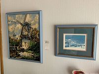 Overall view of both framed pieces, the needlework on the left with light blue frame and the Peter Robson print on the right with dark wooden frame.
